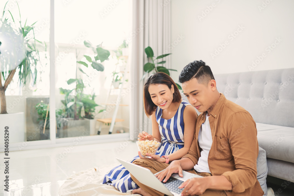 一对年轻的亚洲夫妇在客厅用笔记本电脑看视频