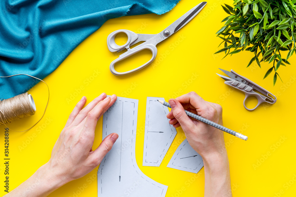 Tailor working. Women hands drawing patterns for clothes on yellow background top-down