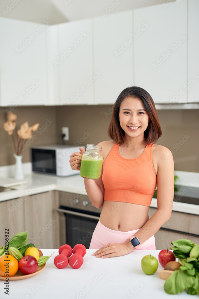 运动型女性站在厨房里喝排毒果汁