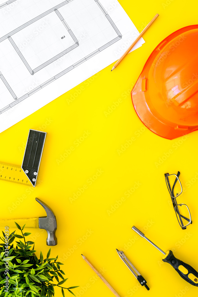 Builder work desk with hard hat, instruments and blueprints on yellow background top-down frame copy