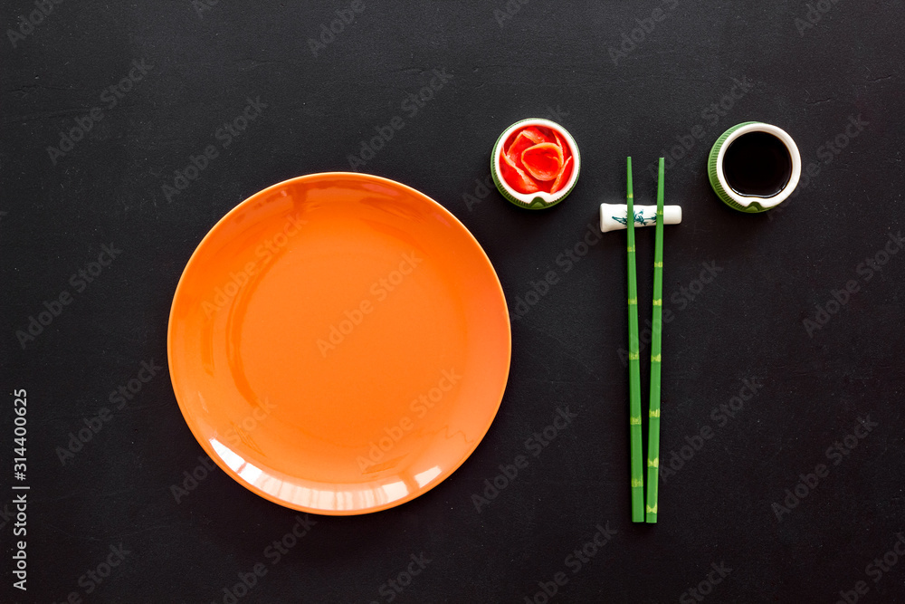 Tableware for sushi and rolls. Plate, chopsticks, small bowls with ginger and sause on black backgro