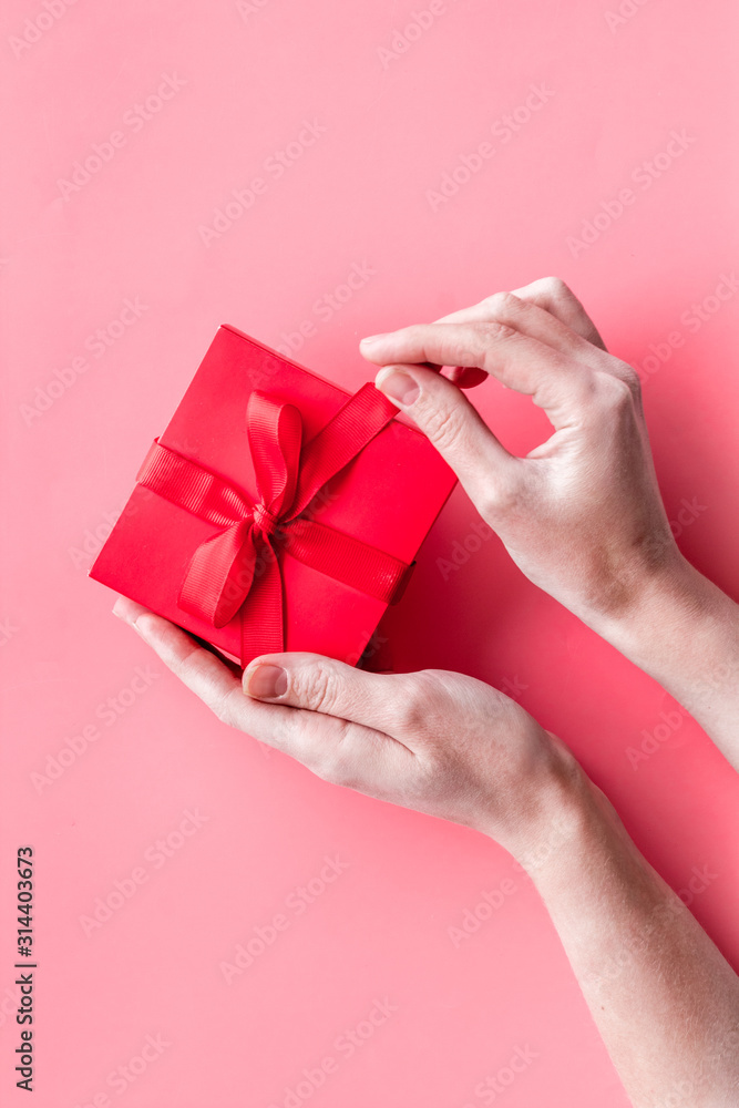 Unpack a gift on Valentines Day. Women hand hold ribbon tied present box on pink background top-dow