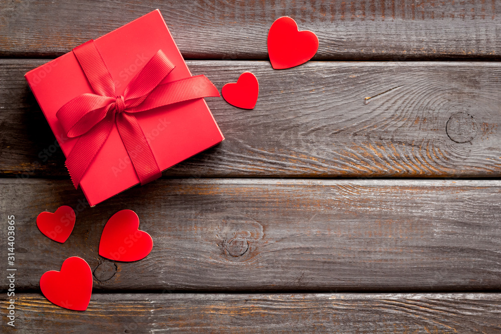 Gift to a sweetheart on Valentines Day. Red present box near hearts on dark wooden background top-d