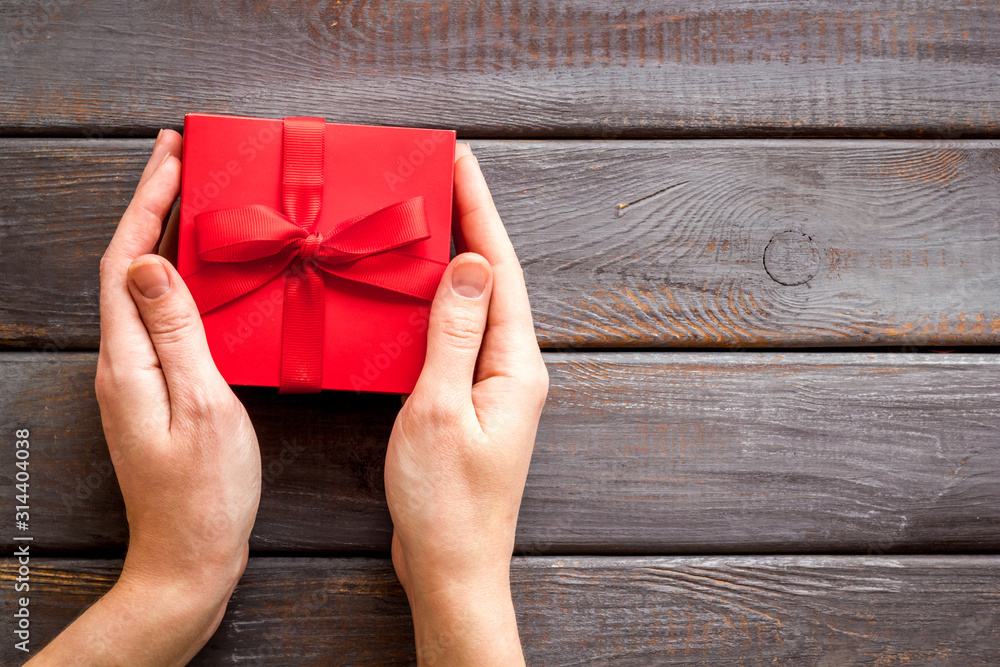 情人节送礼物。女性手持深色木质背景的漂亮红色礼品盒