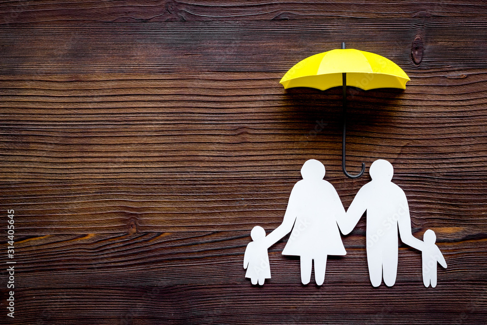 Live insurance concept. Family silhouette protected by umbrella on dark wooden background top-down c