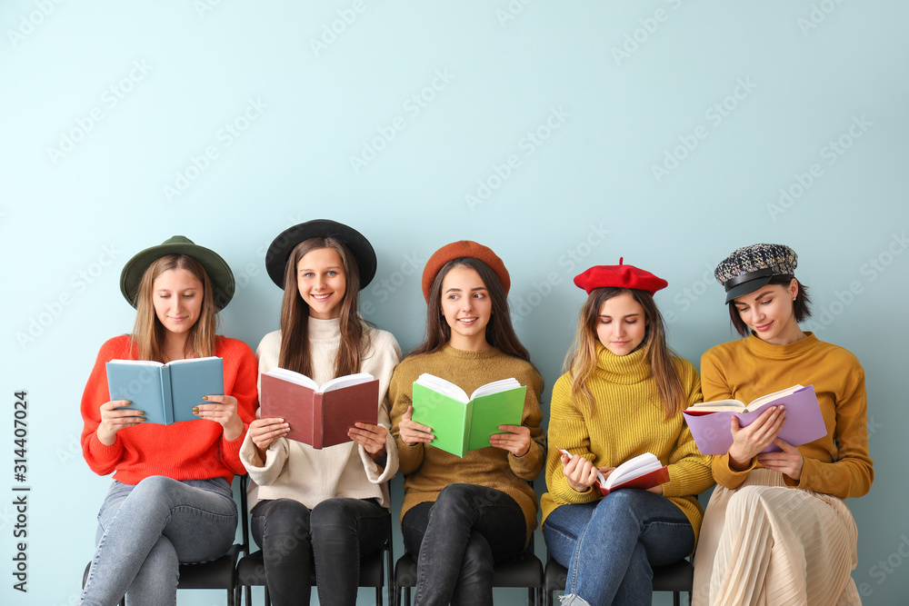 Young women with books sitting near color wall