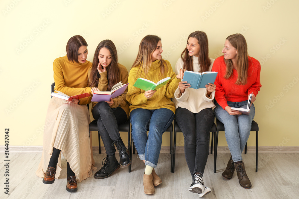 Young women with books sitting near color wall