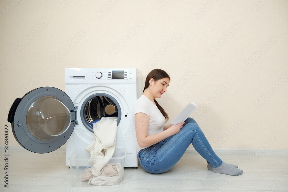 穿着牛仔裤的年轻家庭主妇坐在地板上学习新洗衣机的设置
