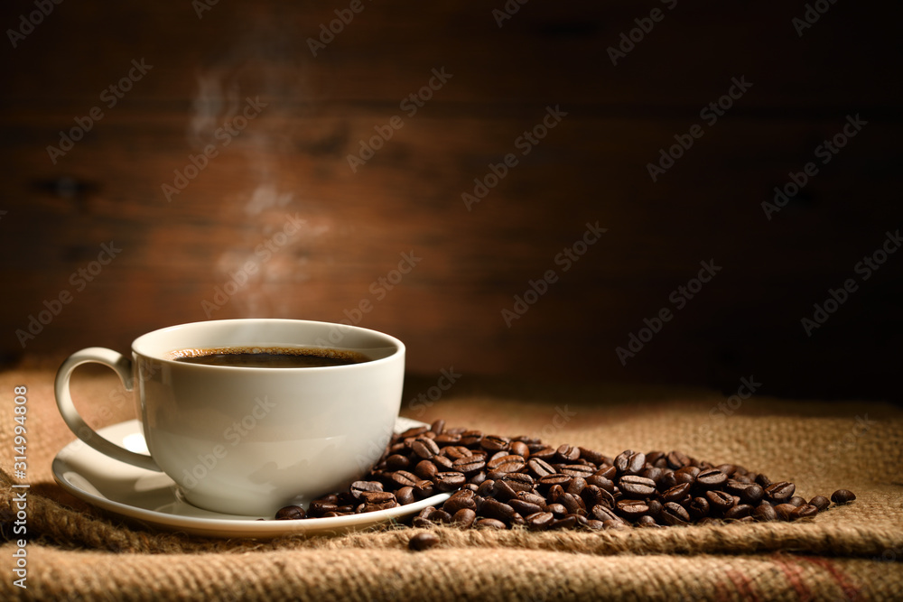 一杯烟熏咖啡，咖啡豆放在旧木背景上的粗麻布袋上