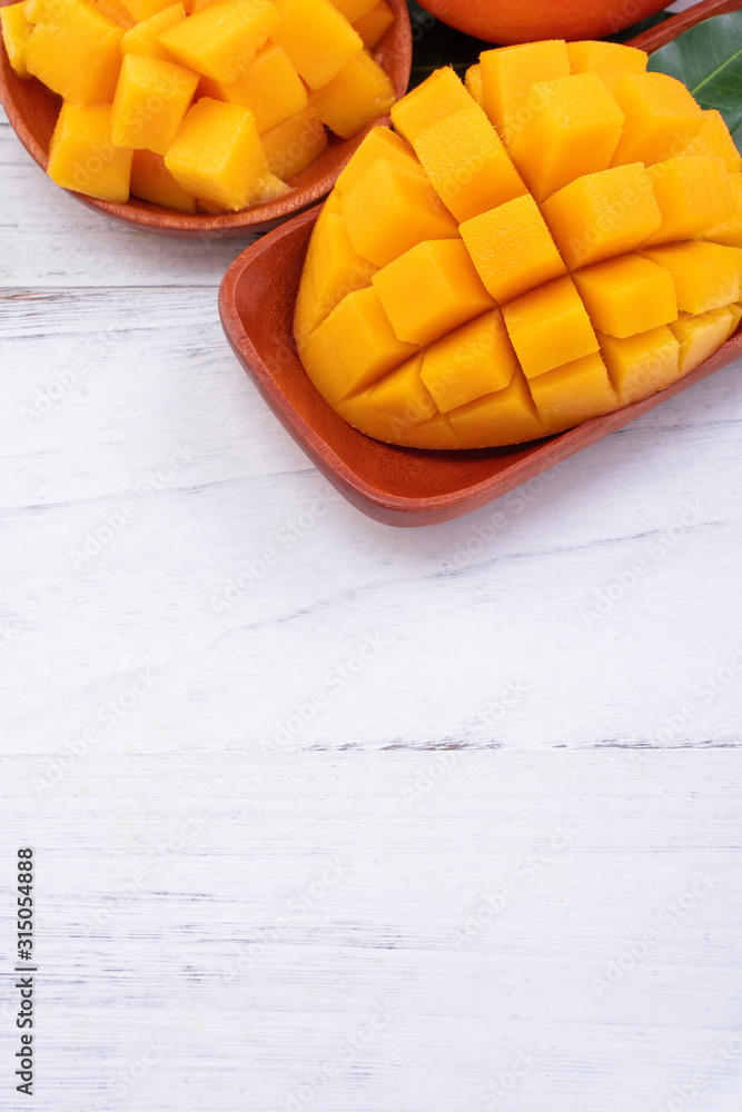 Fresh mango,beautiful chopped fruit with green leaves on bright wooden table background. Tropical fr