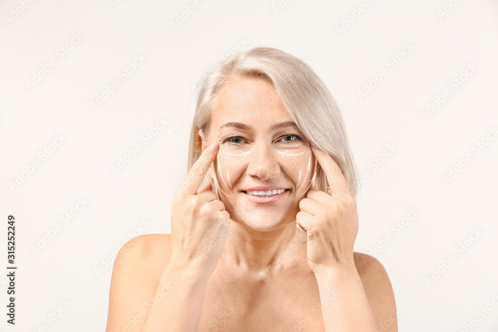 成熟女性在浅色背景下给自己做面部按摩