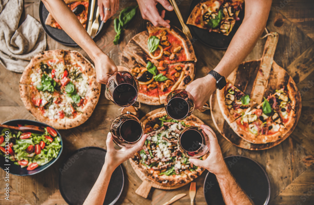 家人或朋友正在吃披萨派对晚餐。人们一边碰杯一边喝红酒。