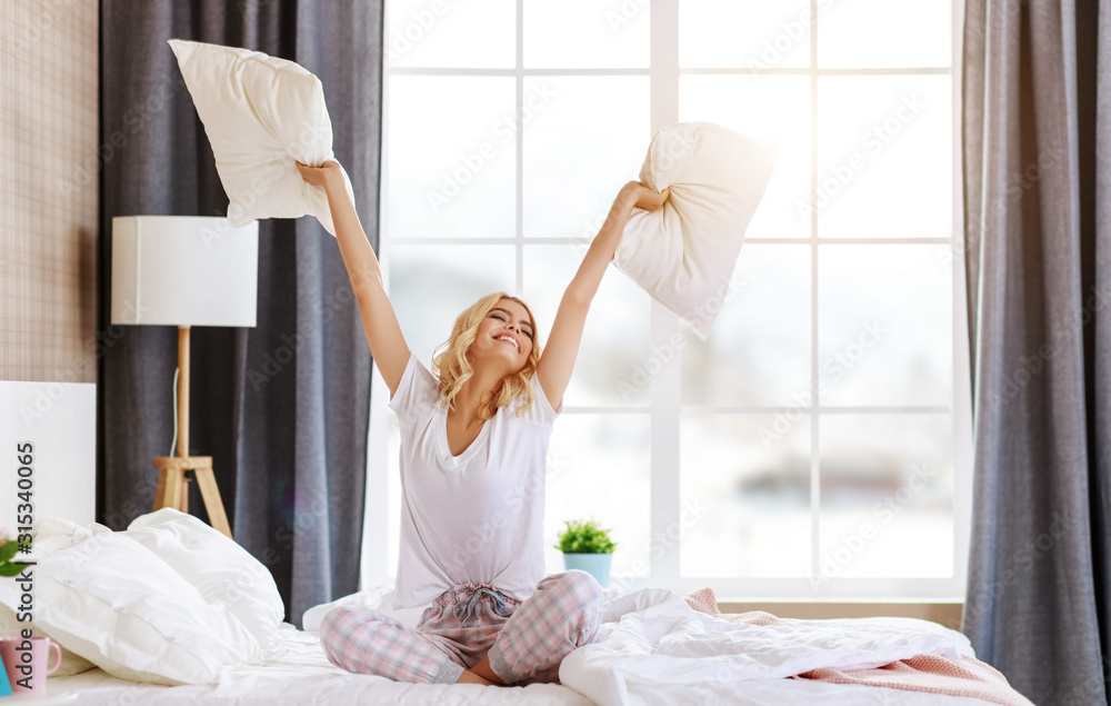 快乐的年轻女人早上在家里的床上笑着跳