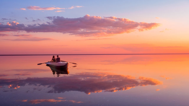 一对相爱的情侣在湖上的划艇上看美丽的日落。粉红色的天空和香草味的云。