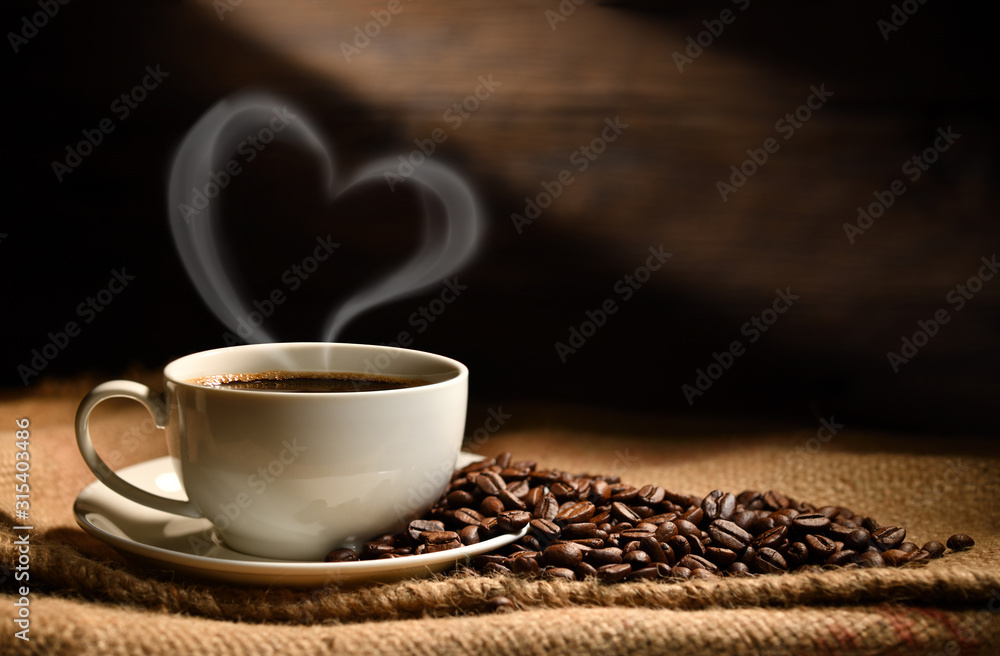 一杯咖啡，心形烟雾，咖啡豆放在旧木背景上的粗麻布袋上