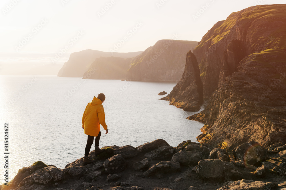 穿着黄色夹克的游客在丹马法罗群岛瓦加岛上的索瓦格斯瓦顿湖附近眺望悬崖