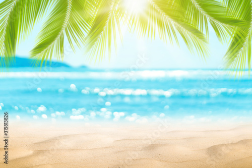 模糊美丽的自然绿色棕榈叶在热带海滩与散景太阳光波抽象背景