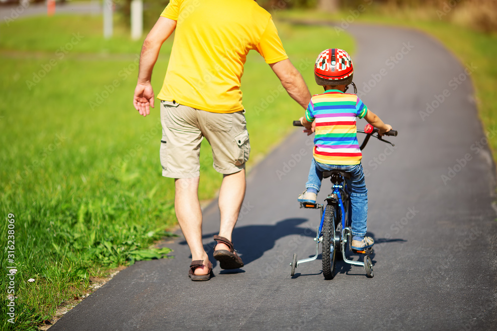 一个戴着头盔骑自行车的孩子和父亲在柏油路上