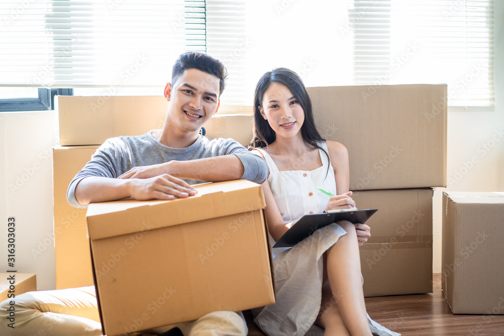 亚洲家庭搬房子的肖像，年轻可爱的女人和帅气的男人拿着箱子坐在地板上