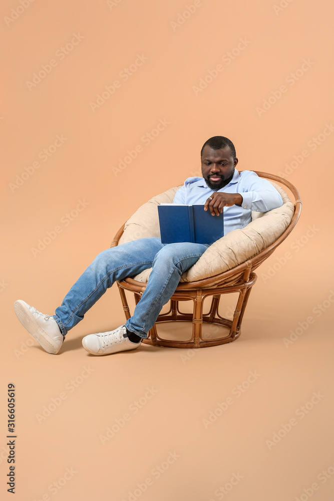 非洲裔美国人坐在扶手椅上看书，背景是彩色的