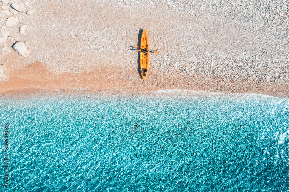 黄色独木舟俯瞰空旷的沙滩，阳光明媚的b海岸有透明的蓝色海水