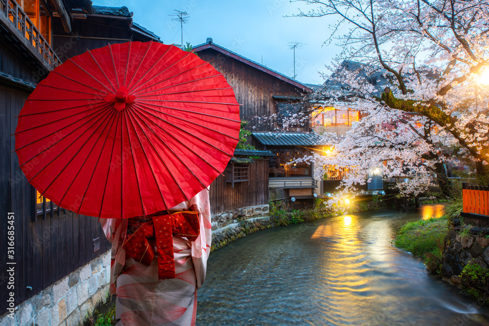 Asian young woman traveller wearing japanese traditional kimono with red umbrella sightseeing at fam