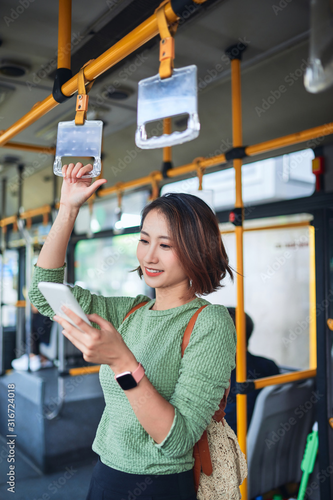 美丽的年轻女子站在城市公交车上看着手机。