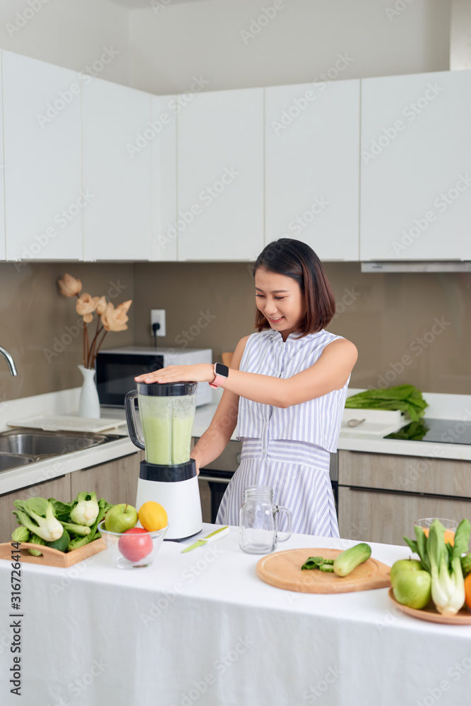微笑的素食亚洲女性在厨房里用水果和蔬菜做奶昔
