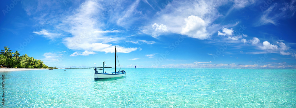 Boat in turquoise ocean water against blue sky with white clouds and tropical island. Natural landsc