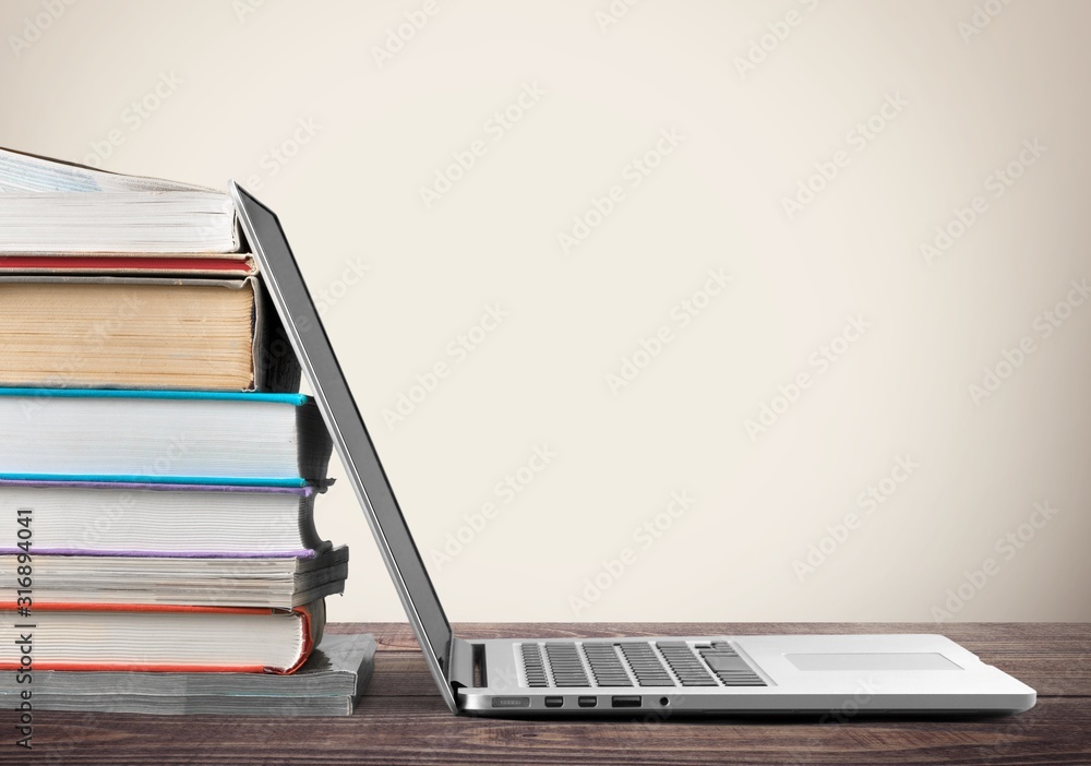 Stack of books with a laptop on wooden table