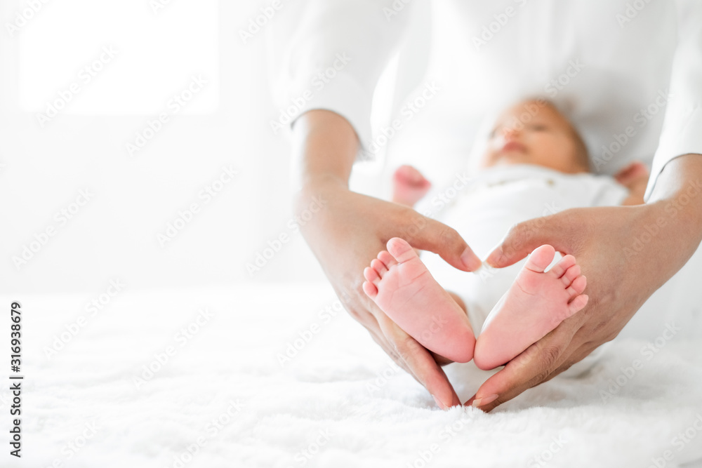 年轻的亚洲母亲在白色床上抱着心形新生儿，母亲节概念