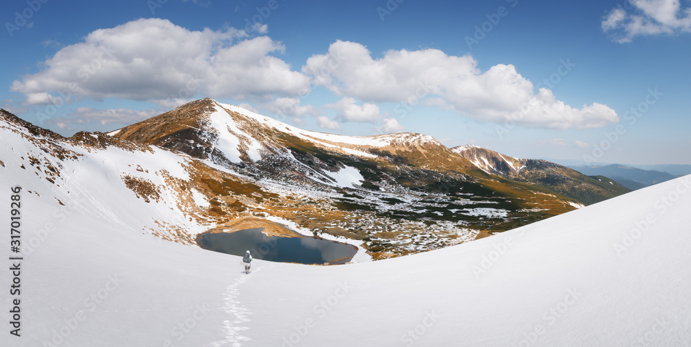 背着背包的游客在春天的山区徒步旅行。冰冻的山湖和悬崖下的雪山