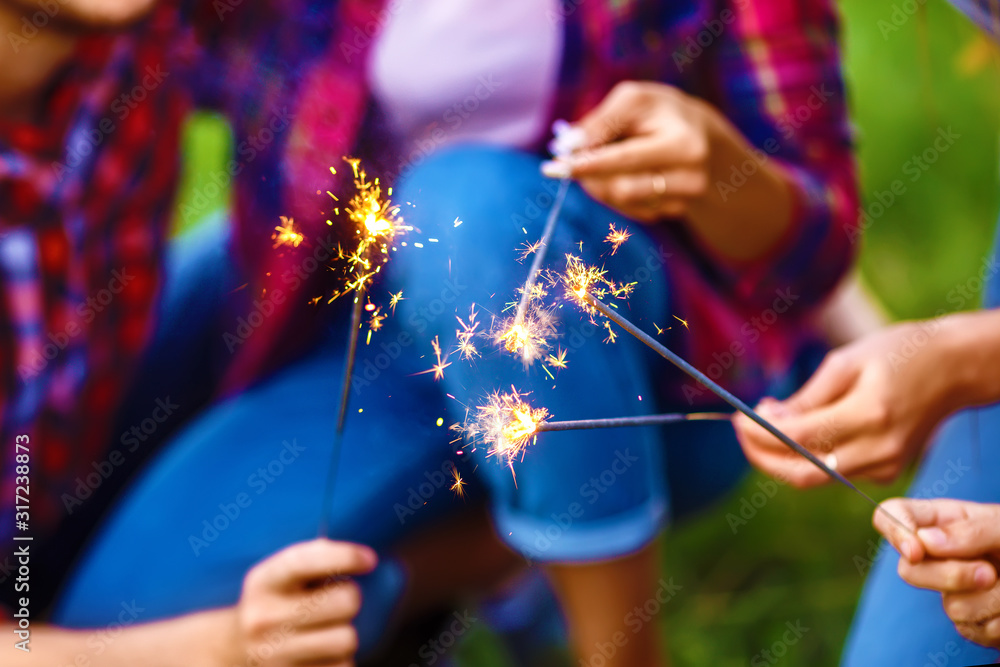 一群朋友坐在夏季公园的草地上玩焰火。青少年玩得很开心