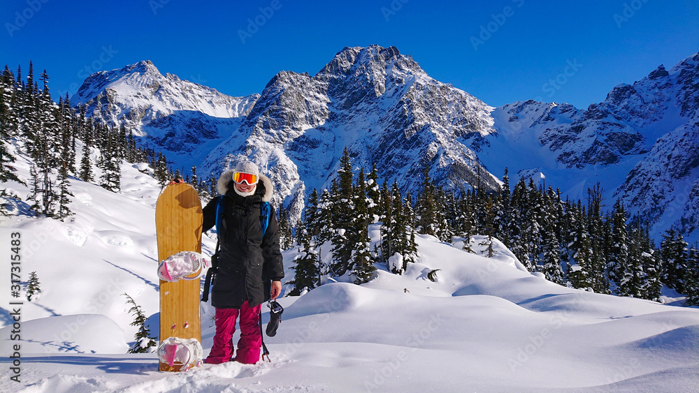 肖像：快乐的女单板滑雪运动员在山前摆姿势时微笑