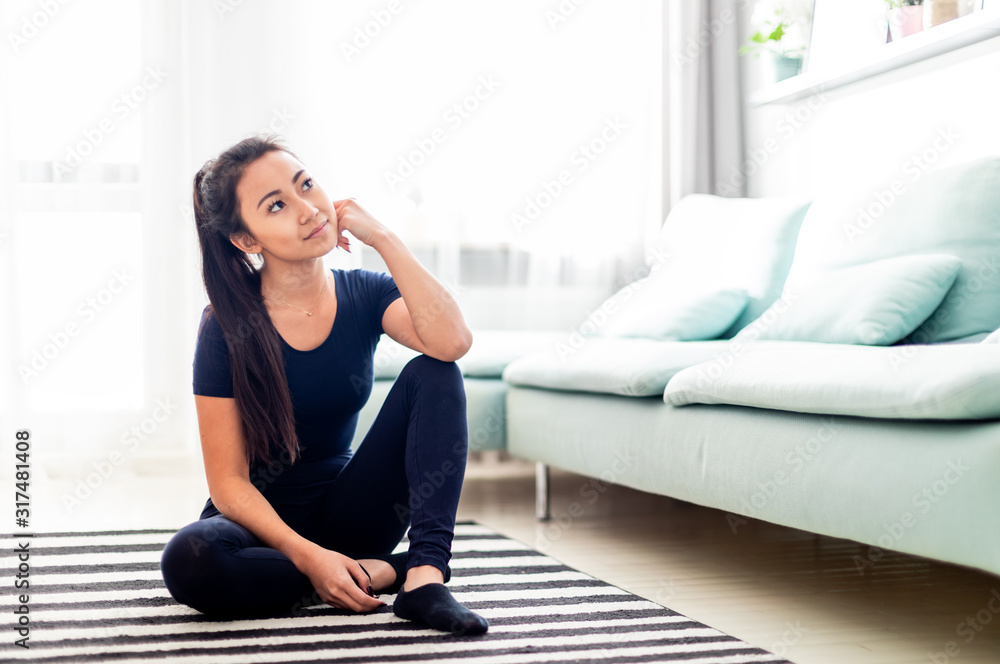 年轻的亚洲女孩坐在家里的地板上思考一些事情