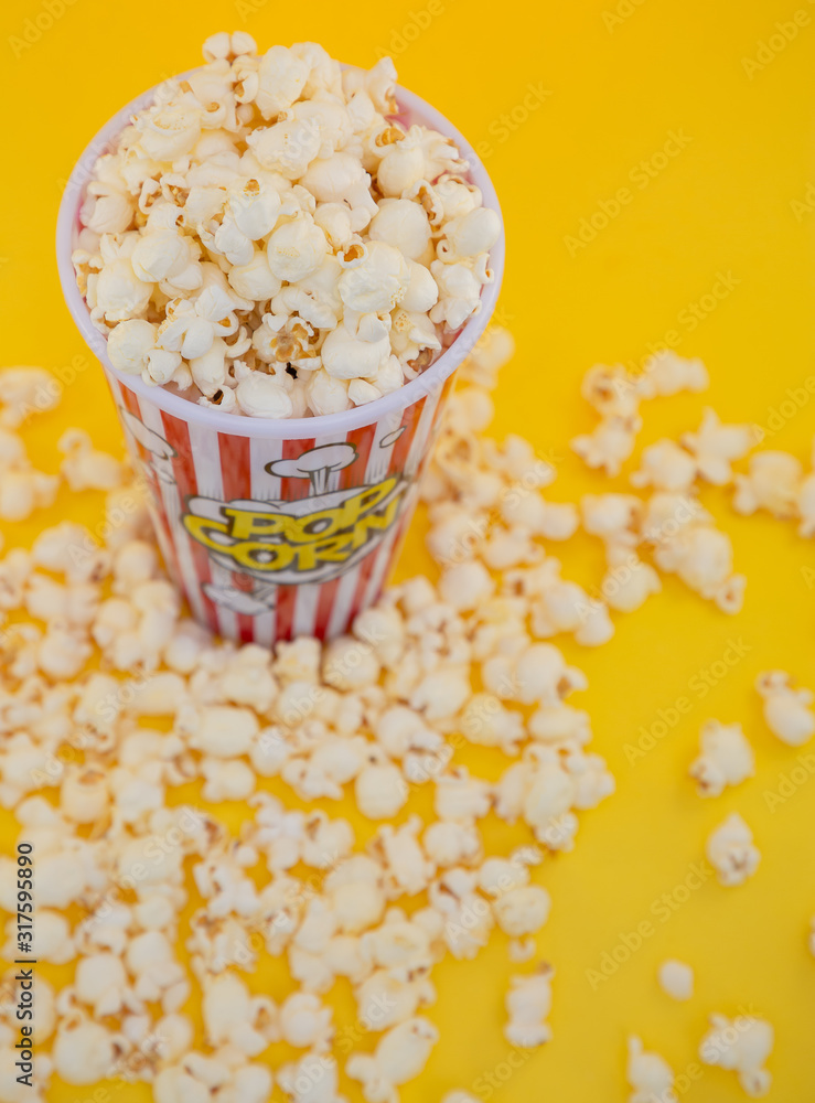 红色爆米花杯中的黄油爆米花，黄色背景下的房子或电影院里的小吃