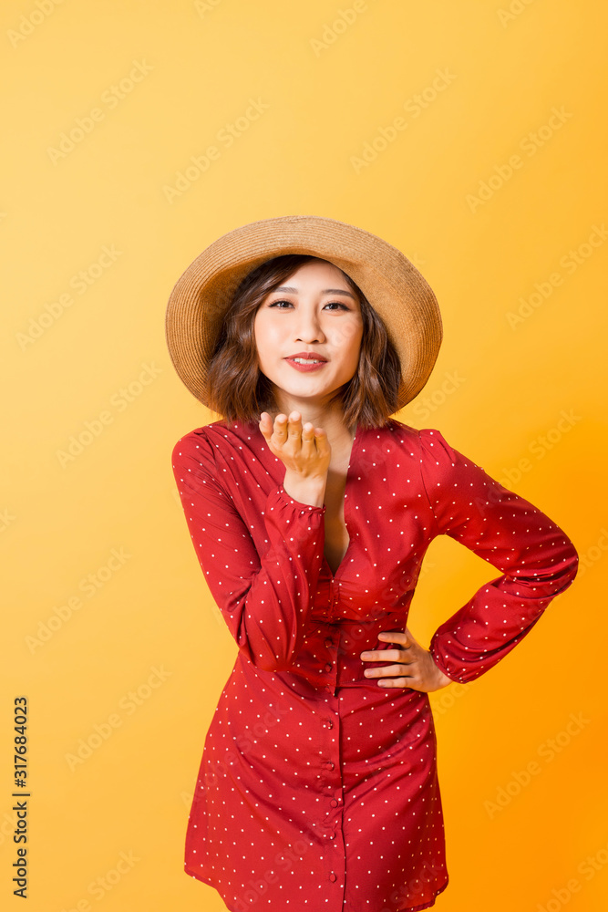 亚洲年轻女子送飞吻。女孩身穿红色连衣裙，棕色帽子，橙色背景