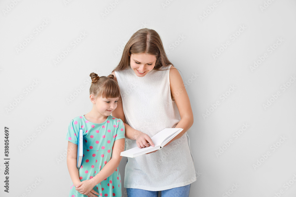 Beautiful young woman and her little daughter with books on light background