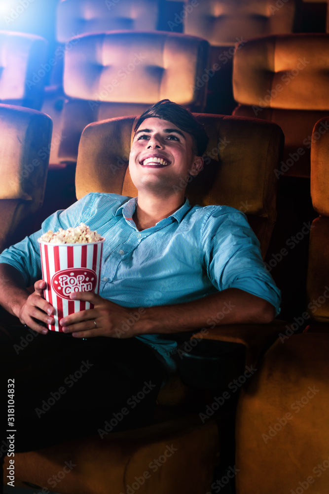 一个年轻人在电影院看电影时，微笑着享受着爆米花