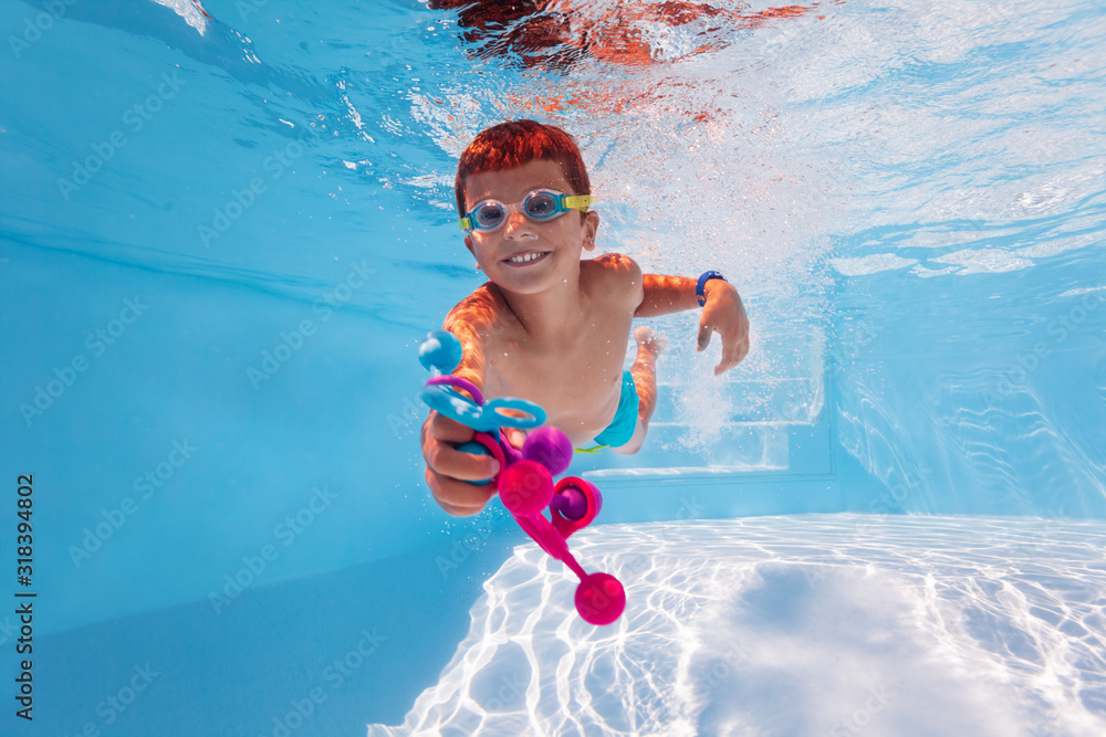 可爱的快乐男孩在游泳池里游泳，穿着谷歌收集五颜六色的玩具