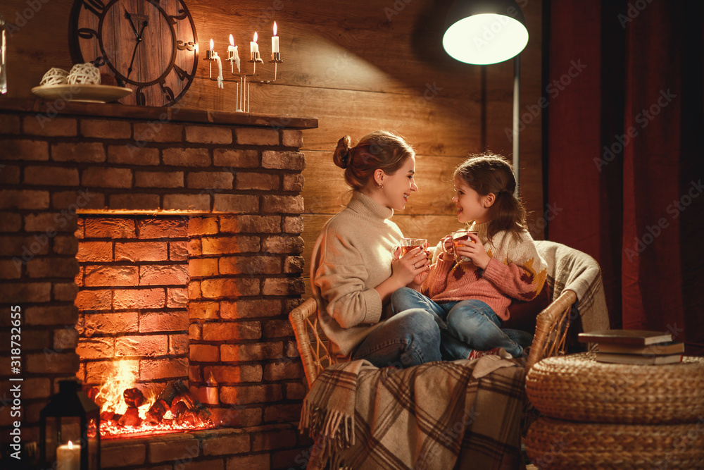 家庭母亲和孩子在冬天的晚上在壁炉旁看书喝茶