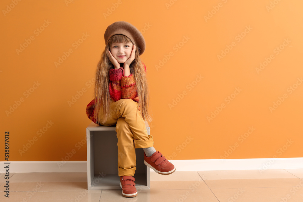 穿着秋装的可爱小女孩坐在彩色墙上