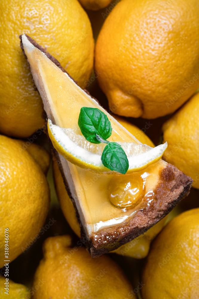 Lemon cheesecake slice with fresh mint leaf and yellow ripe lemons on the background. Beautiful, del