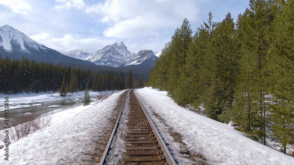 空中：沿着锈迹斑斑的火车轨道飞行，穿过白雪覆盖的松林。