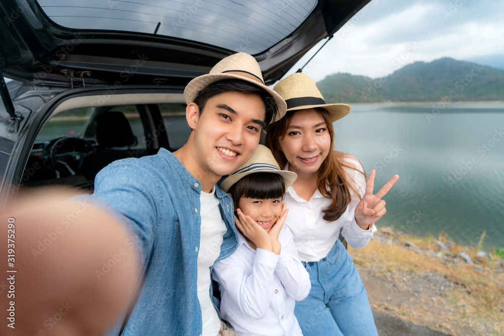 Portrait of Asian family sitting in car with father, mother and daughter selfie with lake and mounta