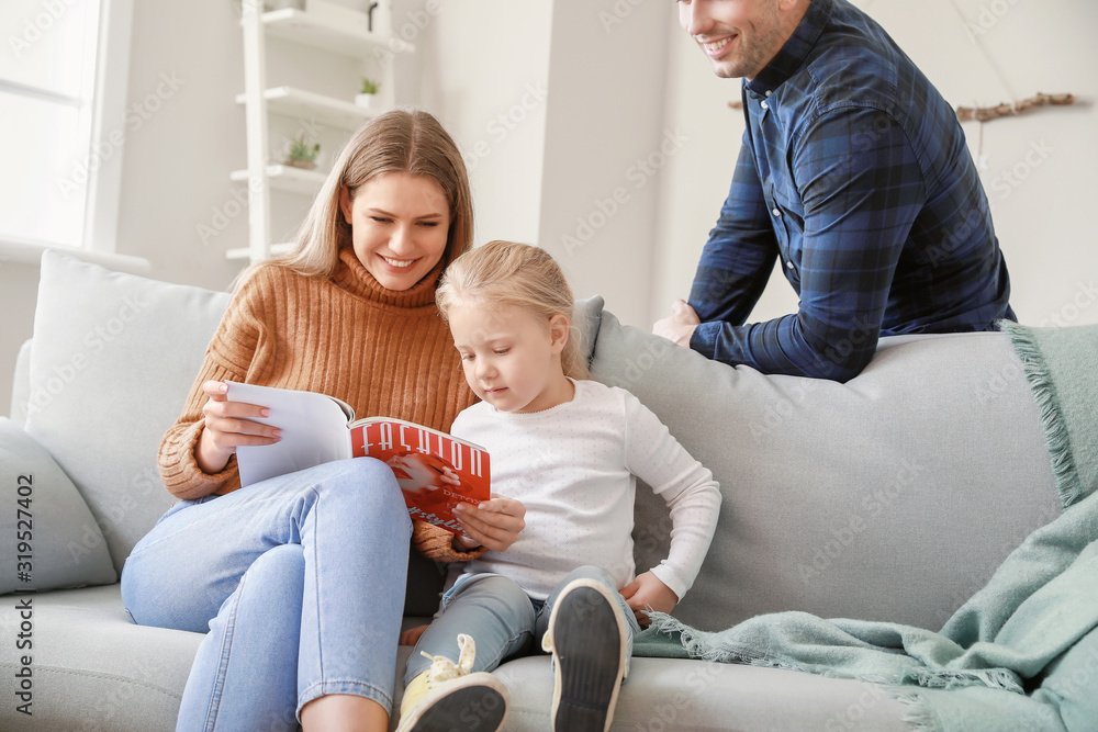 快乐的年轻家庭坐在家里的沙发上阅读时尚杂志