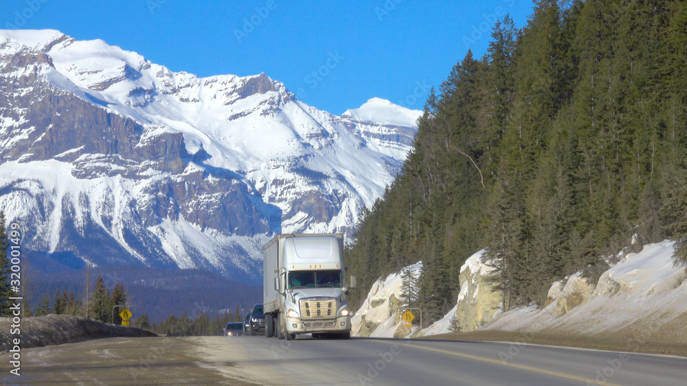 Big 18 wheeler and cars drive down the famous Icefields Parkway on a sunny day.