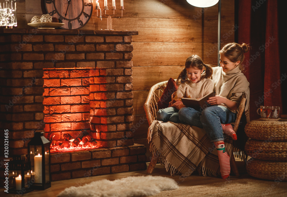 family mother and child reading book and drink tea on winter evening by fireplace