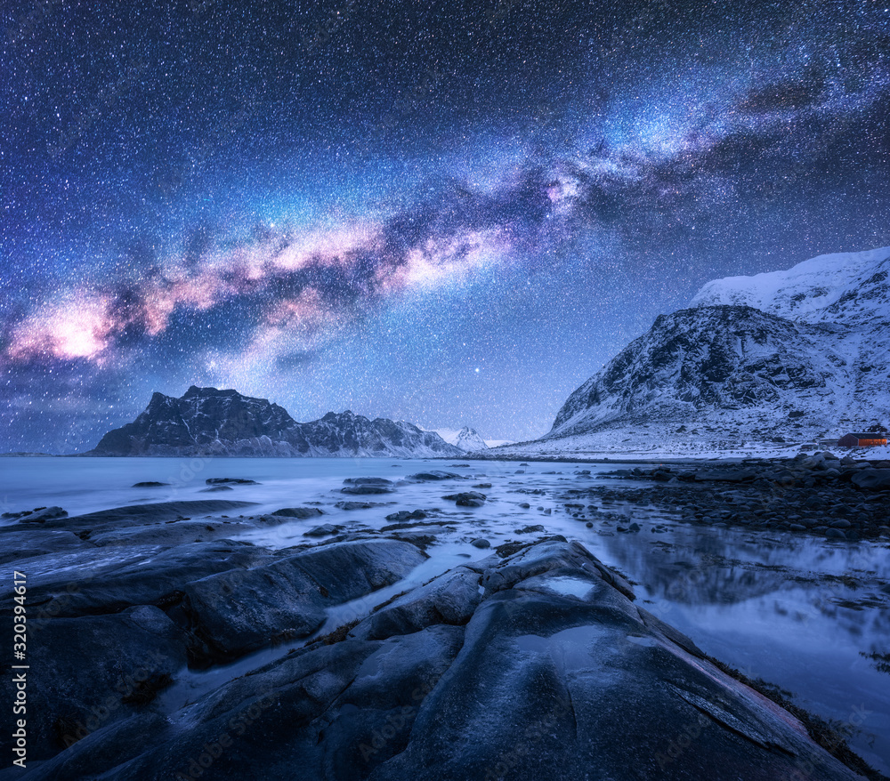 Milky Way above snow covered mountains and rocky beach in winter at night in Lofoten Islands, Norway