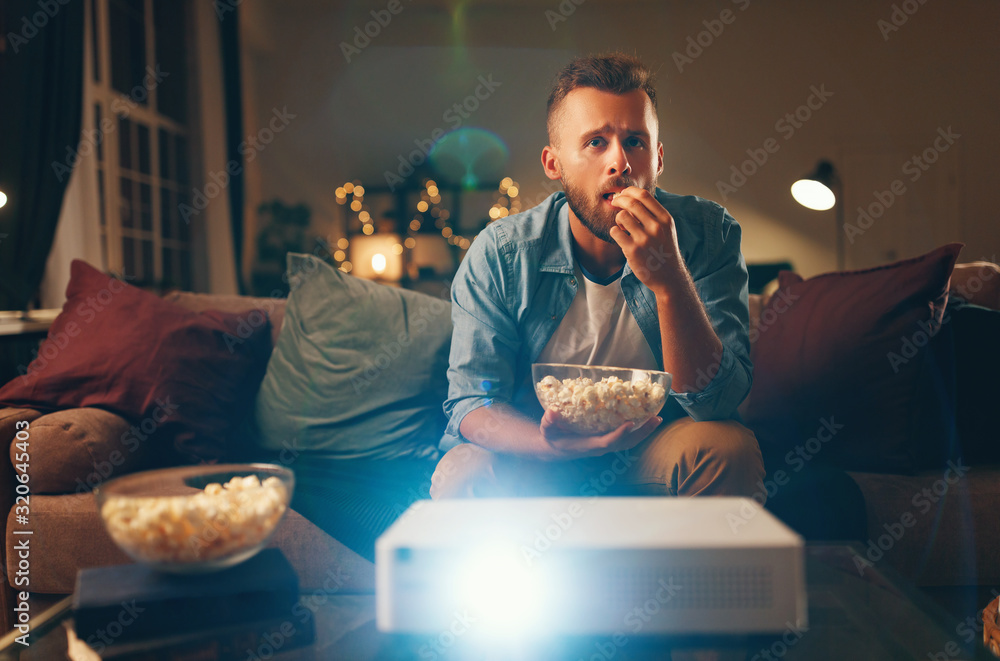 一个年轻人晚上独自在家看投影电视。